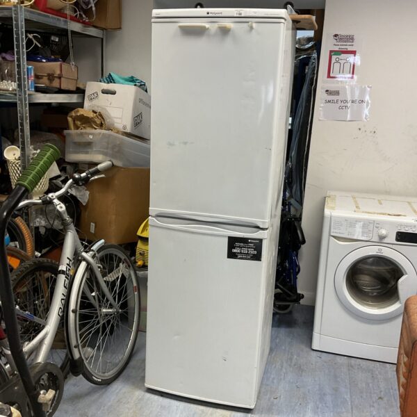White Hotpoint fridge freezer in a cluttered space.