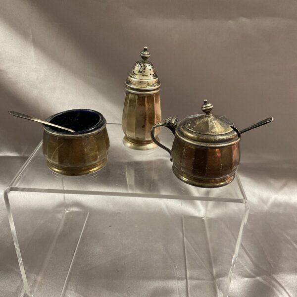 Antique silver mustard, salt, and pepper set on a clear stand.
