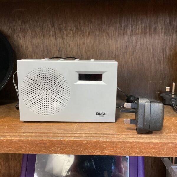 Sandy grey Bush DAB radio with power supply on a shelf.