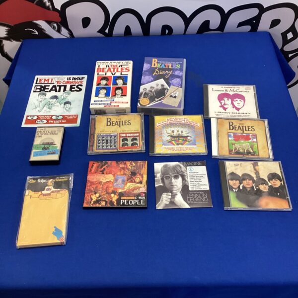 Beatles memorabilia lot featuring CDs, VHS tapes, and a tin sign.