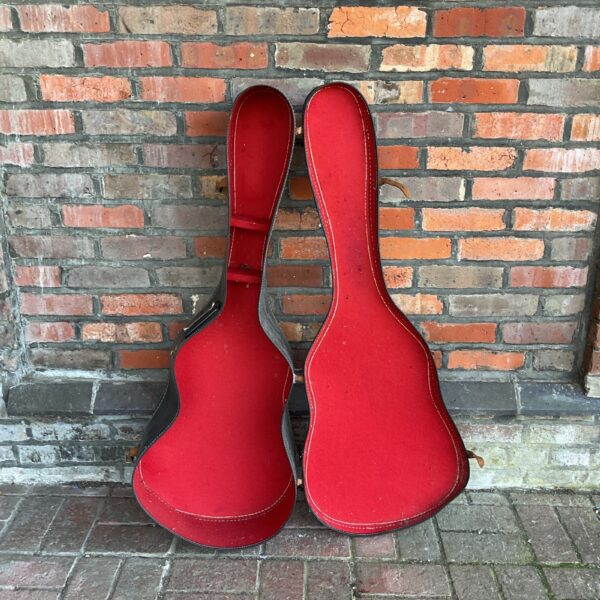 Two vintage red acoustic guitar cases leaning against a brick wall.