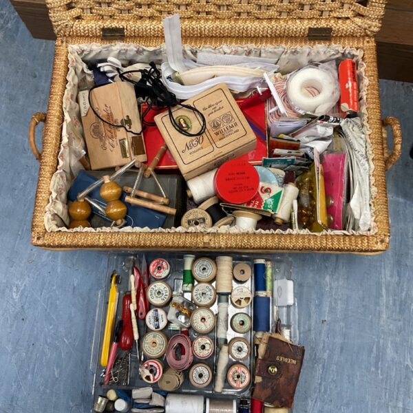 Vintage sewing basket overflowing with antique sewing supplies.